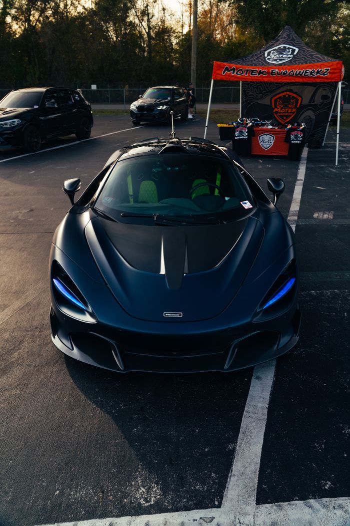 A sleek black sports car displayed outdoors with a vibrant backdrop.
